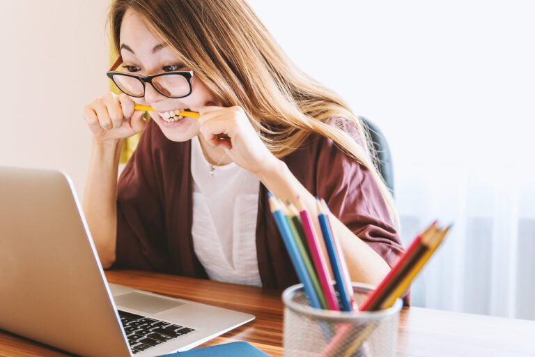 mulher mordendo lápis enquanto olha pro computador